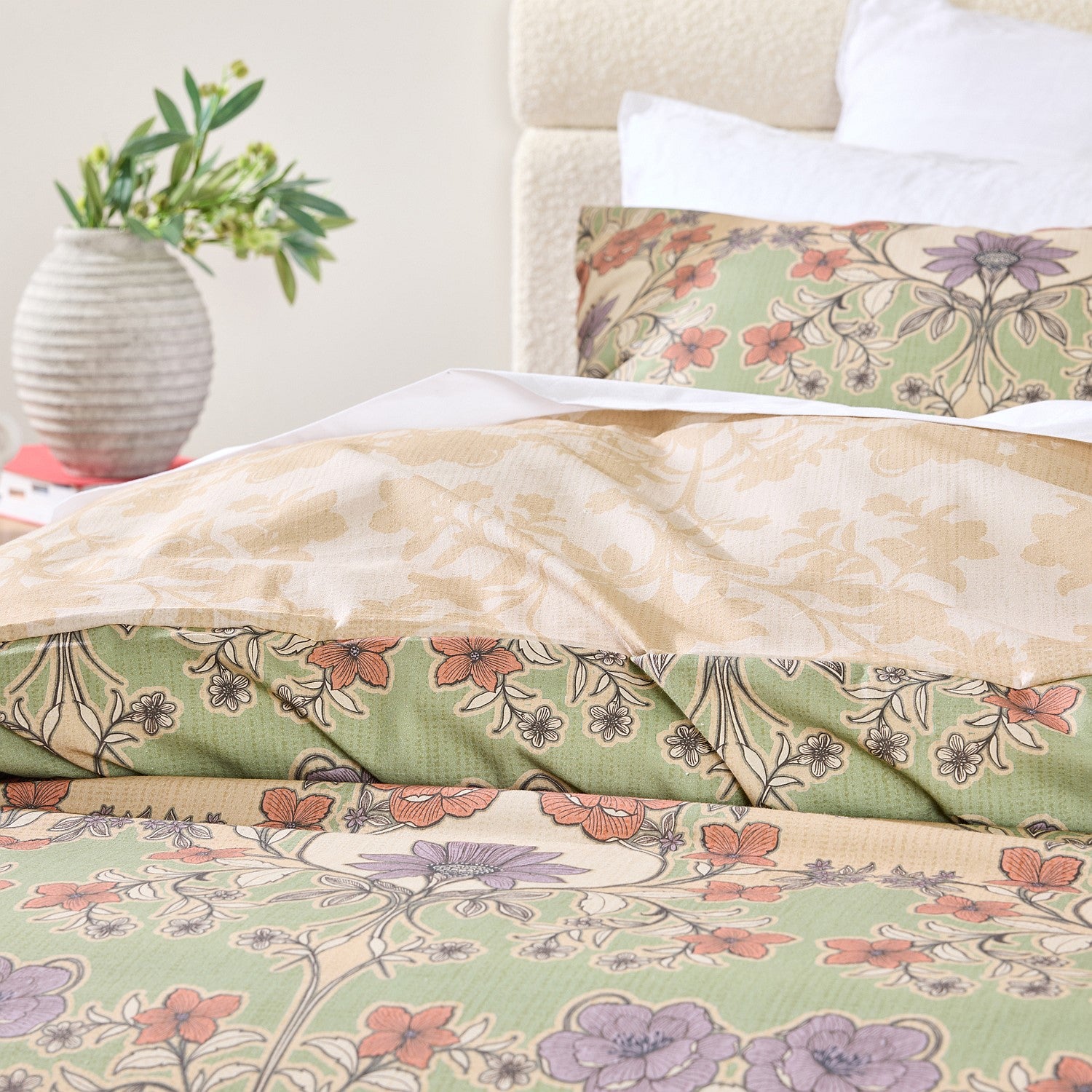 Floral patterned bedding set on a bed with a vase of flowers in the background.