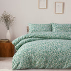 Teal floral duvet set on a bed in a bedroom with a wooden side table and decorative items.