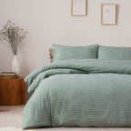 Green striped bedding set on a bed in a bedroom with a side table and decor.