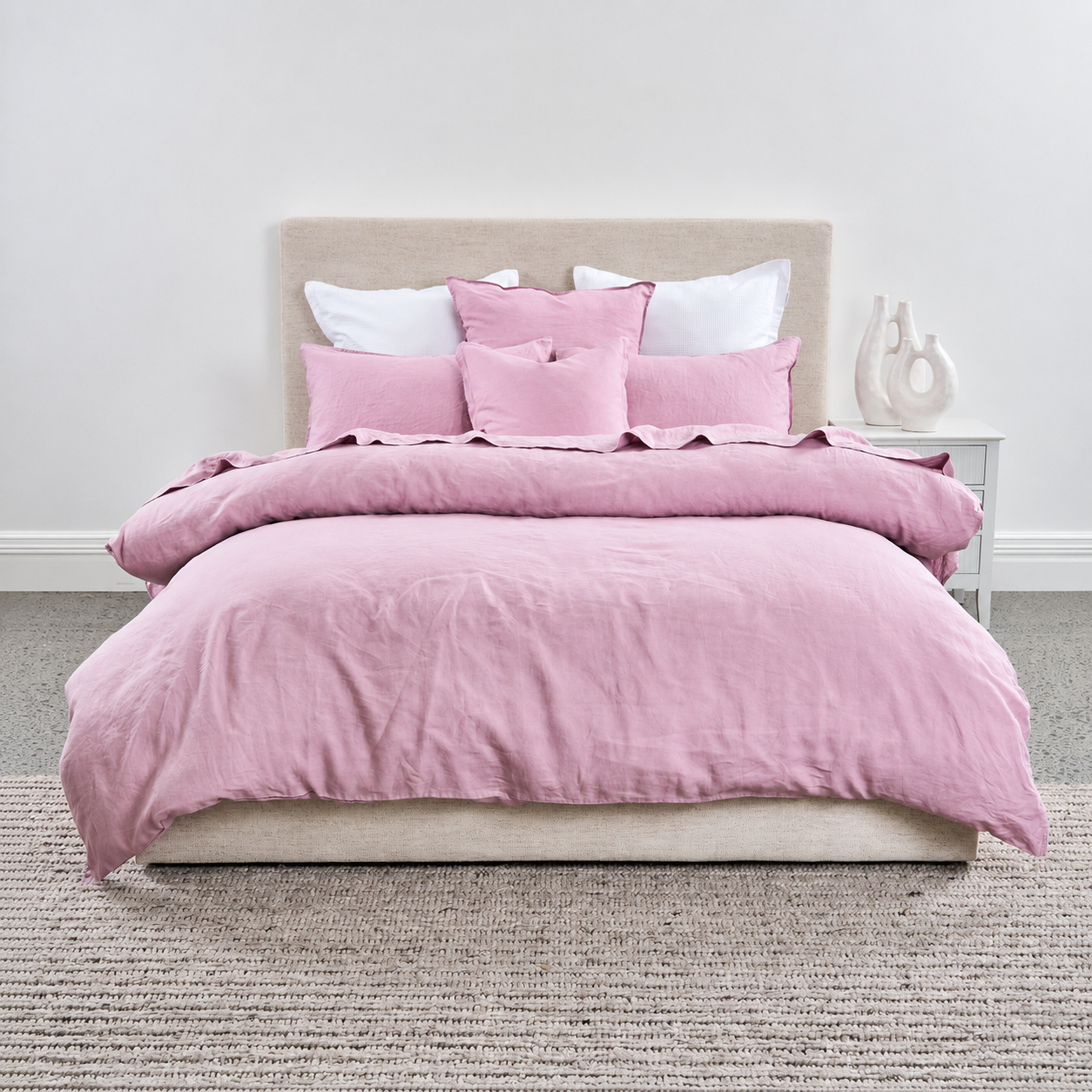 Pink bedding set on a bed with white pillows in a minimalistic bedroom.