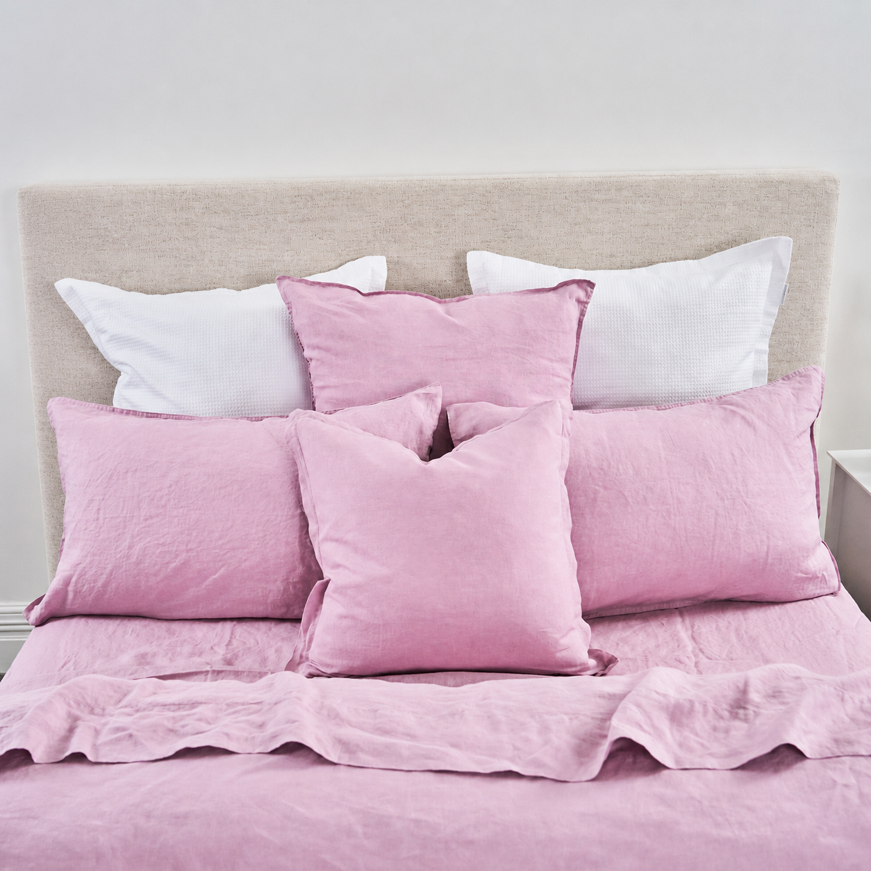 Pink bedding set with pillows on a bed against a white wall.