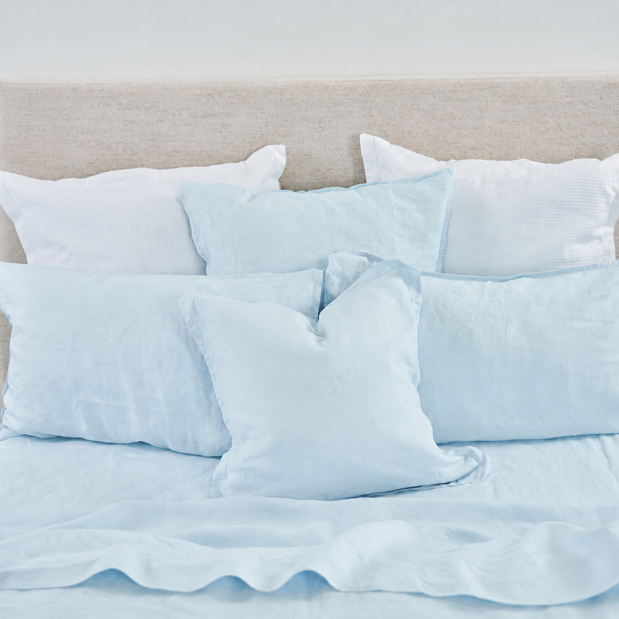 Light blue bedding set on a bed with a neutral headboard.