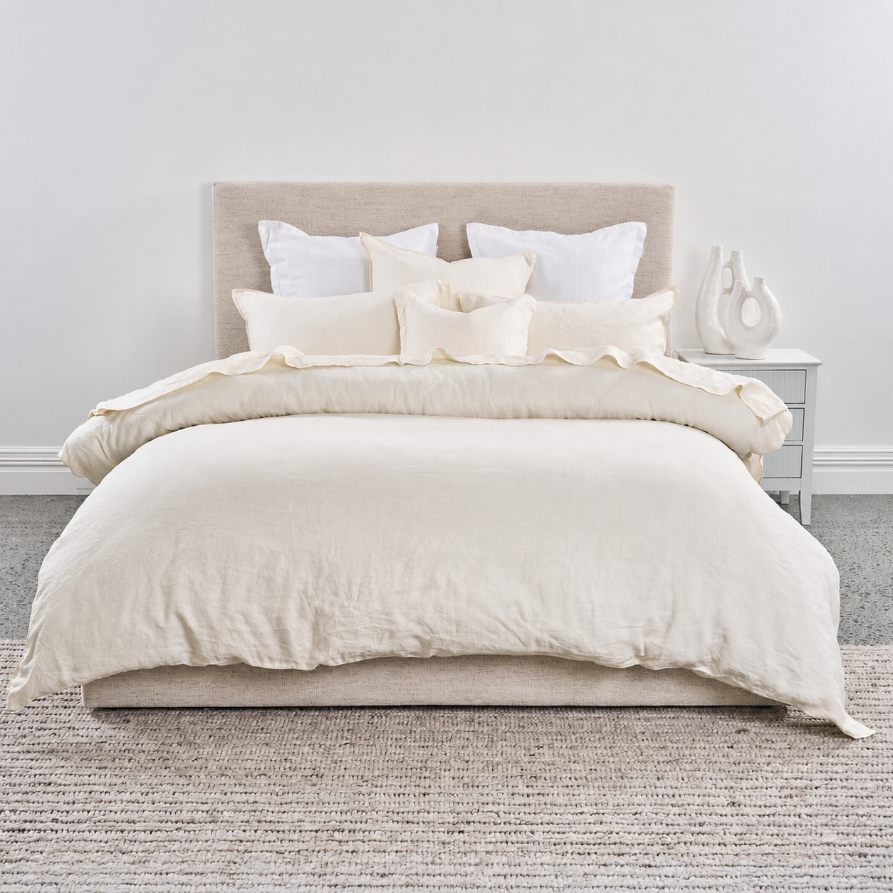 Neatly made bed with beige bedding and pillows in a minimalistic bedroom.