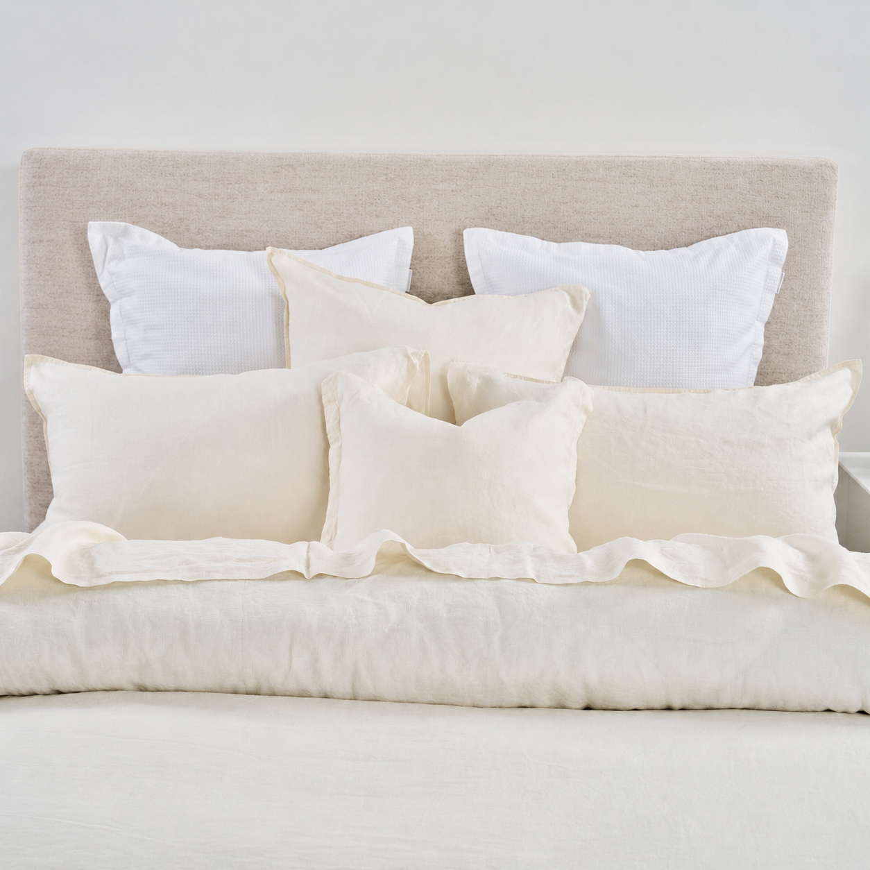 Neatly arranged pillows on a bed with a neutral headboard.
