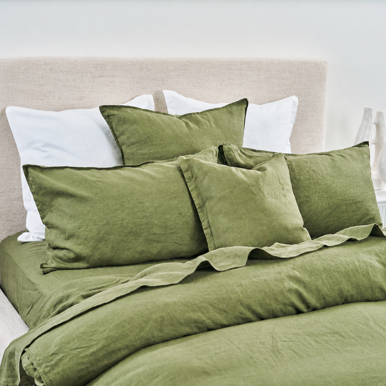 Green bedding set with white pillows on a bed with beige headboard.