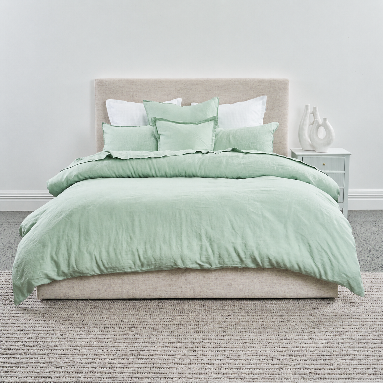 Bed with green bedding and white pillows in a room with a neutral color scheme.