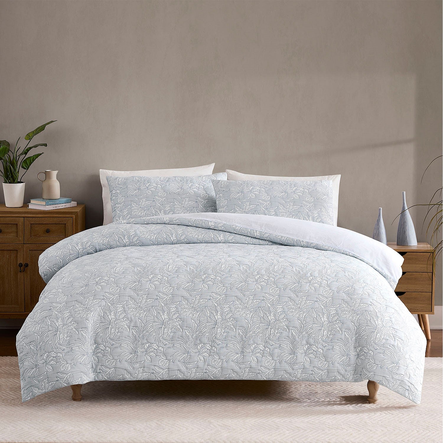 Bed with light blue floral patterned comforter and pillows in a bedroom setting.