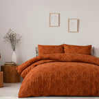 Orange textured bedding set on a bed in a bedroom with a vase and books on a side table.