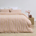 Yellow and pink striped duvet cover set on a bed with a vase of flowers on a nightstand.