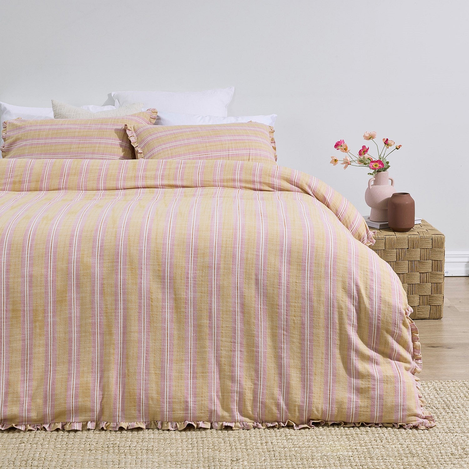 Yellow and pink striped duvet cover set on a bed with a vase of flowers on a nightstand.