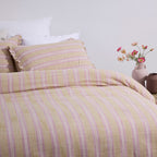 Bed with yellow and pink striped bedding, white pillows, and a vase of flowers on a nightstand.