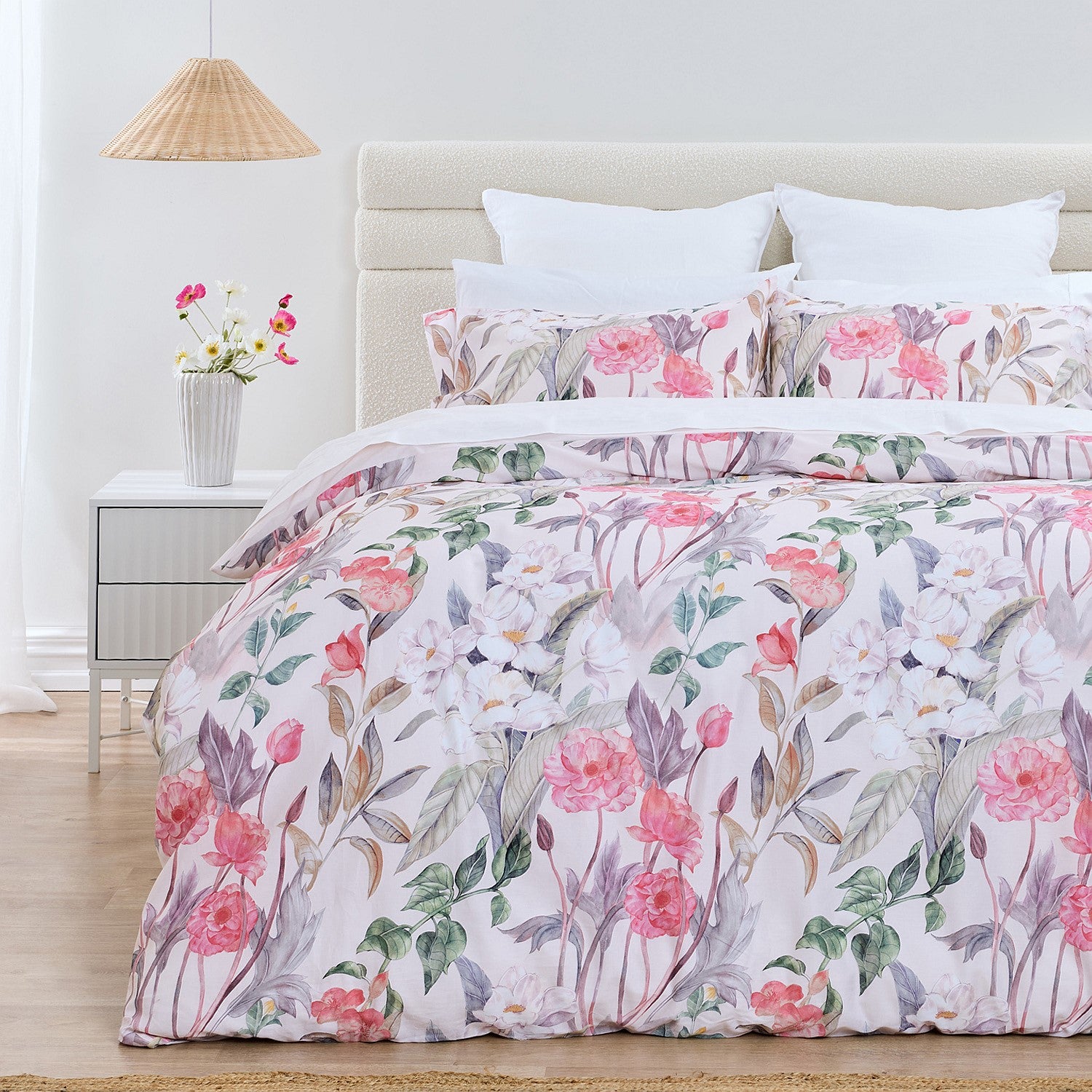 Floral bedding set on a bed in a bedroom with a lamp and flowers on a nightstand.