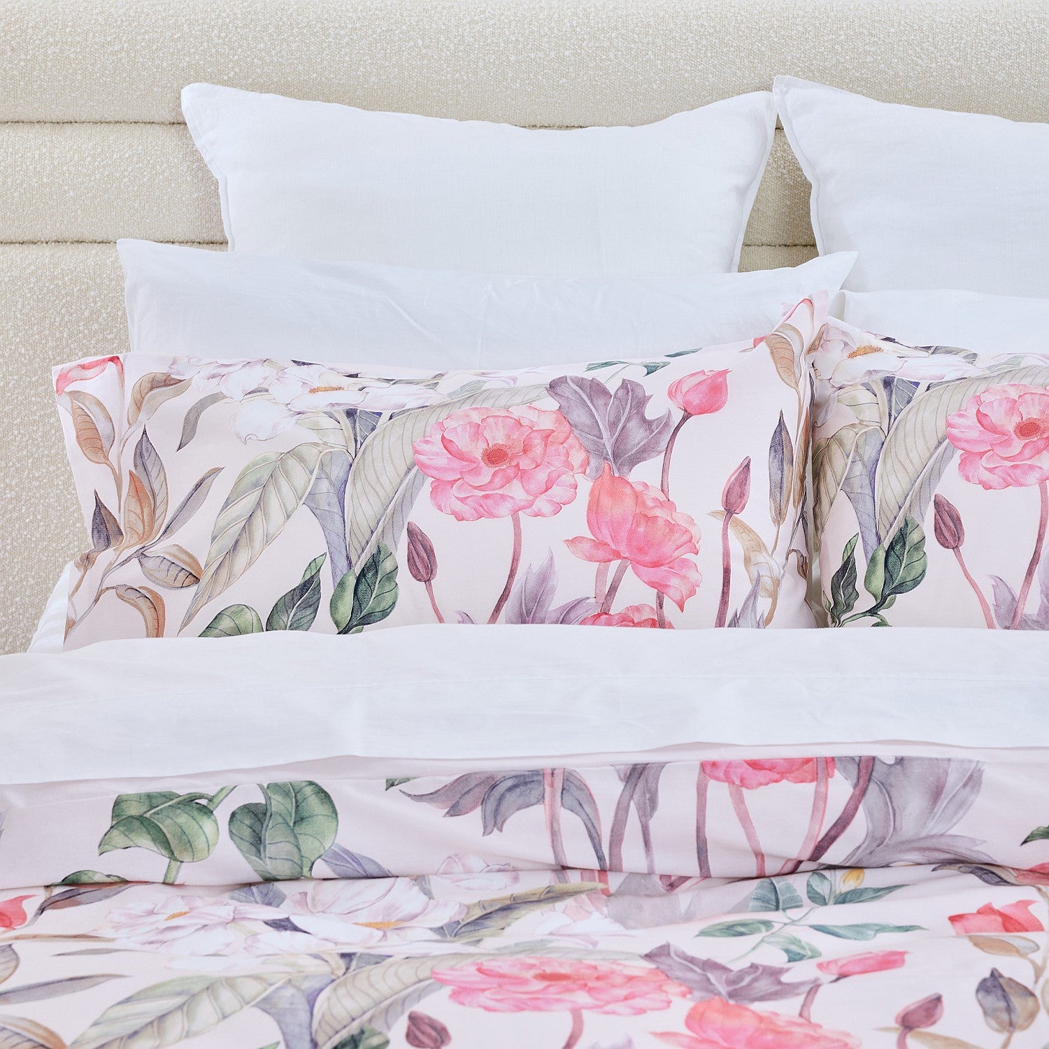 Floral bedding set with pink flowers and green leaves on a bed with white pillows.