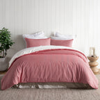 Pink duvet cover set on a bed with white pillows in a room with a plant and side table.
