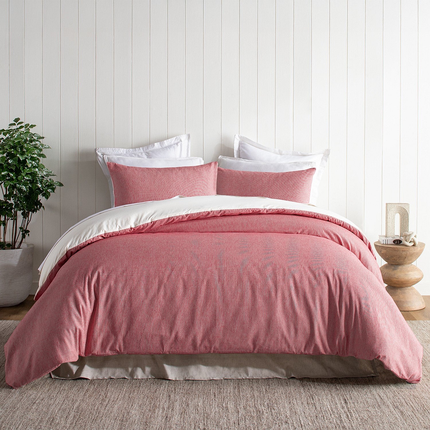 Pink duvet cover set on a bed with white pillows in a room with a plant and side table.