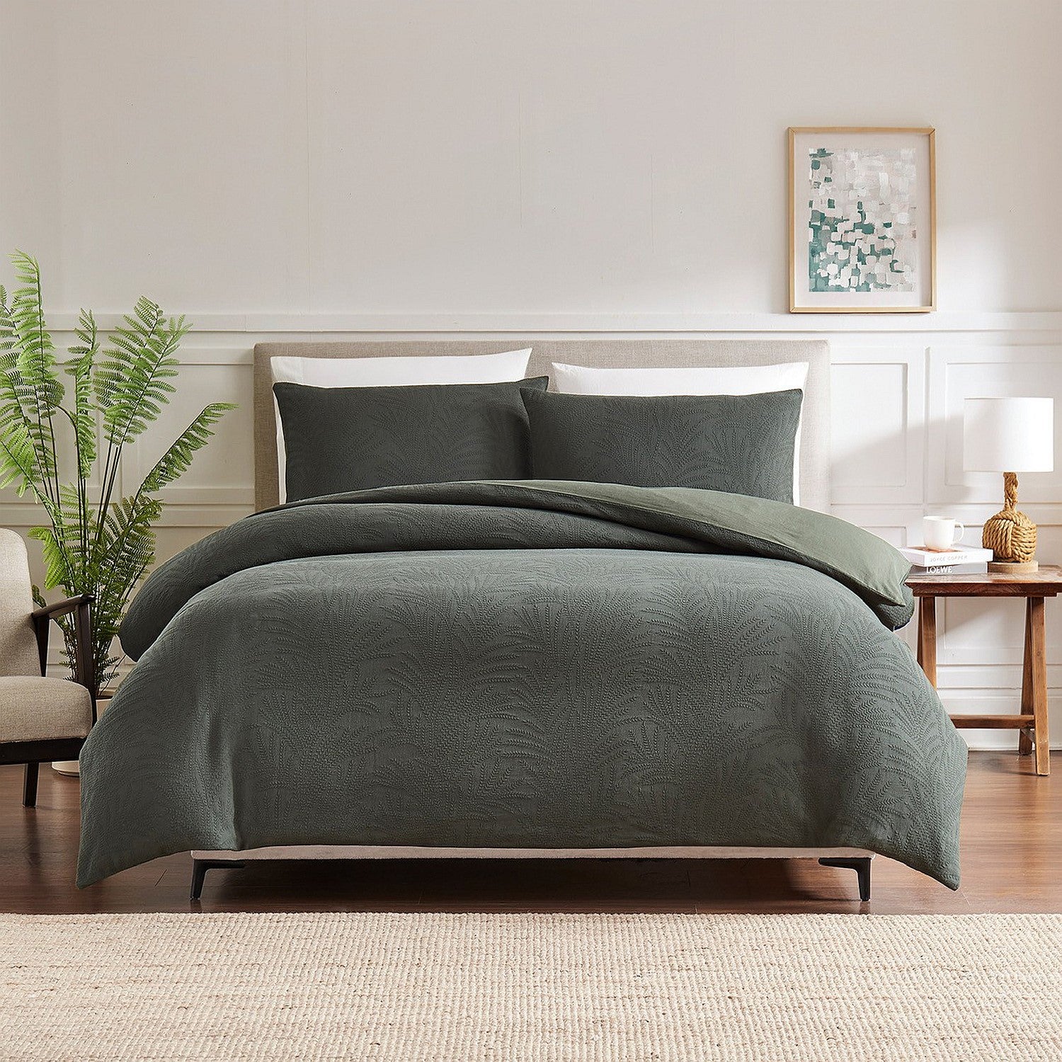 Green bedding set on a bed in a bedroom with a plant and lamp in the background.