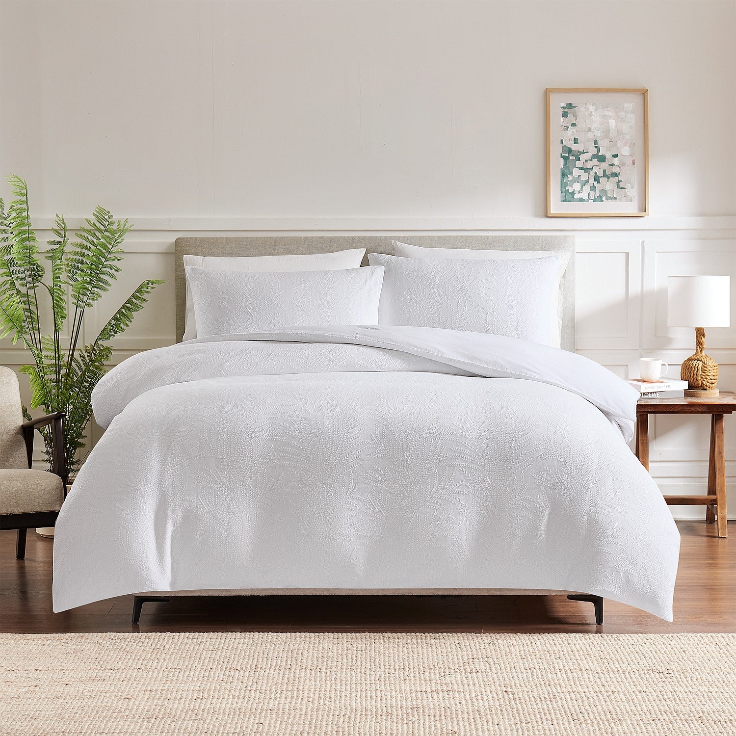 White bedding set on a bed in a bedroom with a plant and side table.