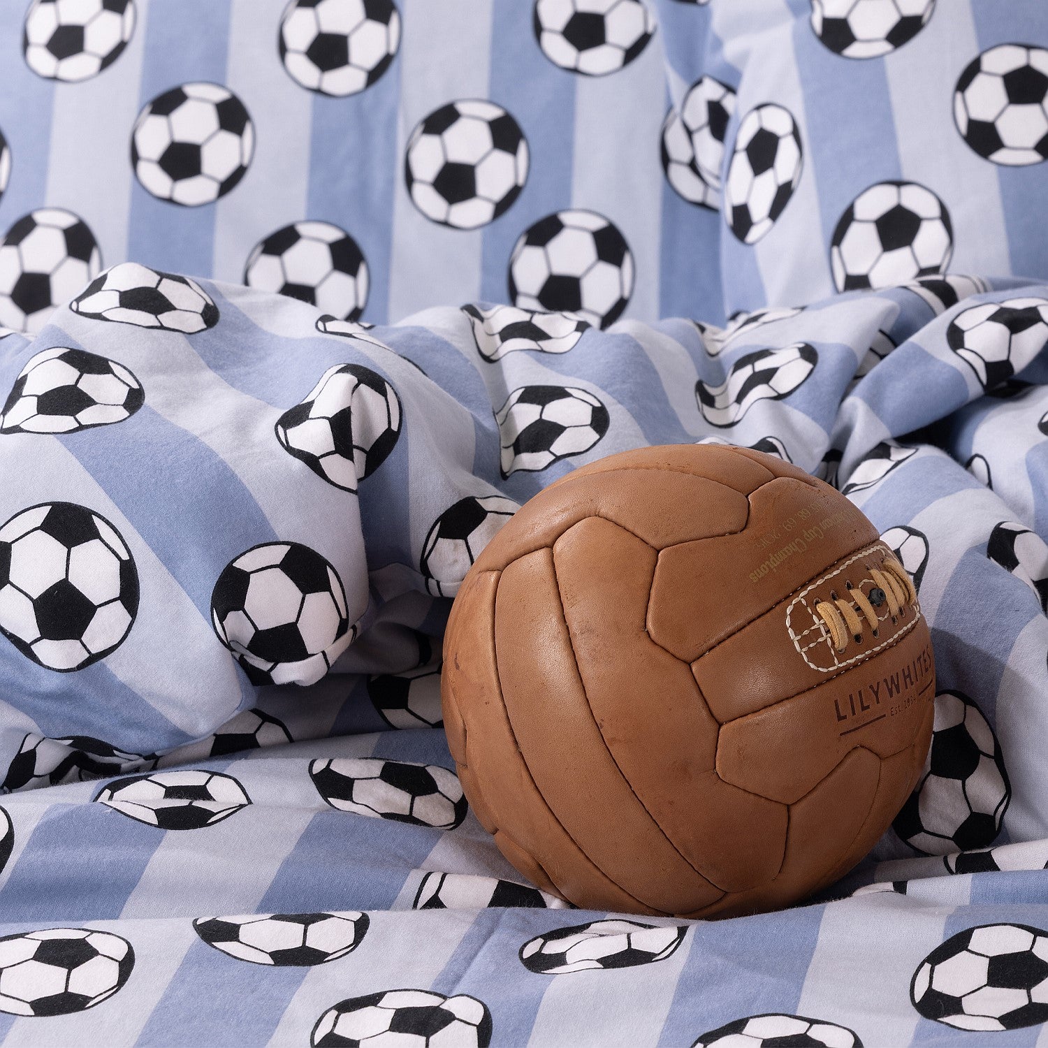 Soccer ball print kids duvet cover set styled with a brown toy ball on the bed.