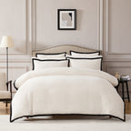 Neatly made bed with white bedding and black trim in a bedroom setting.