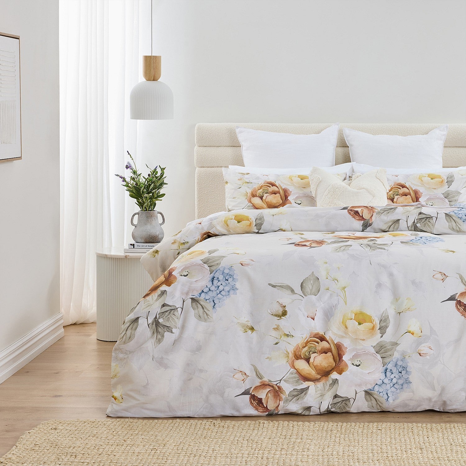 Floral bedding set on a bed in a bedroom with a vase of flowers on a nightstand.