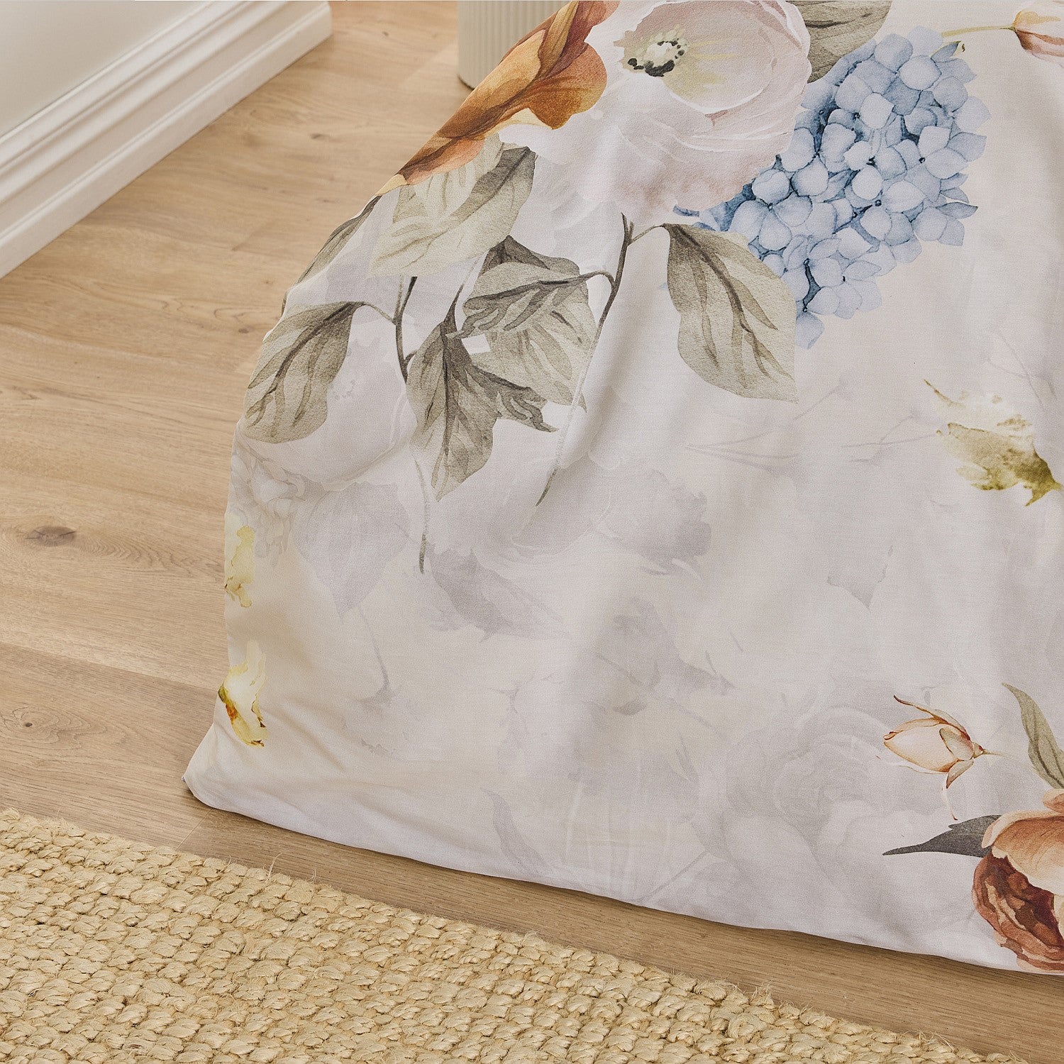 Floral-patterned comforter on a bed with a wooden floor and rug in the background