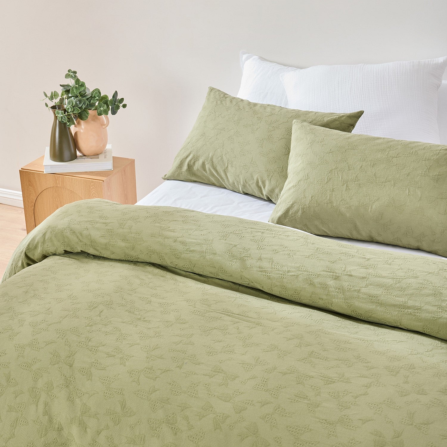 Green bedding set on a bed with a nightstand and plant in the background