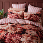 Floral bedding set with striped pillows on a bed against a maroon panel wall.