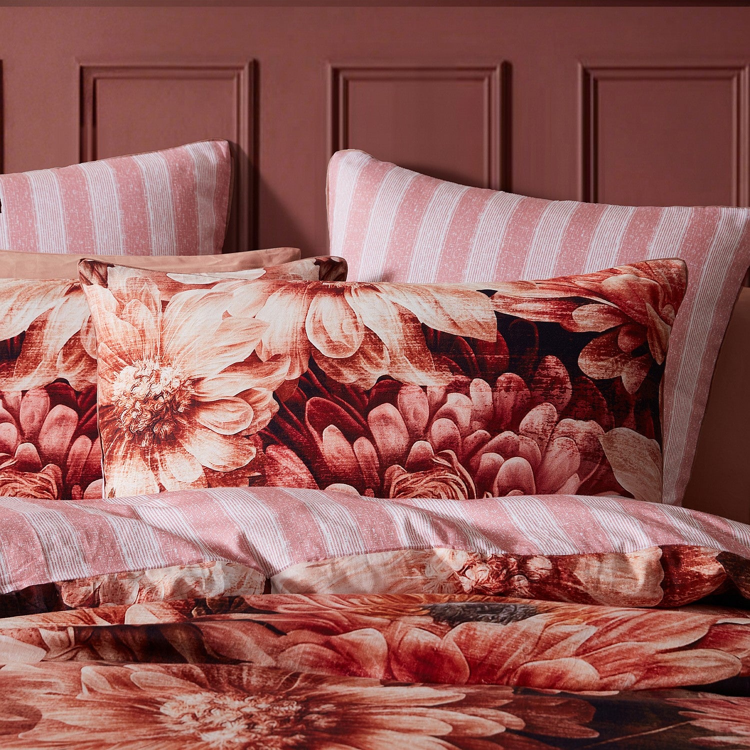 Floral and striped pillows on a bed against a maroon wall.