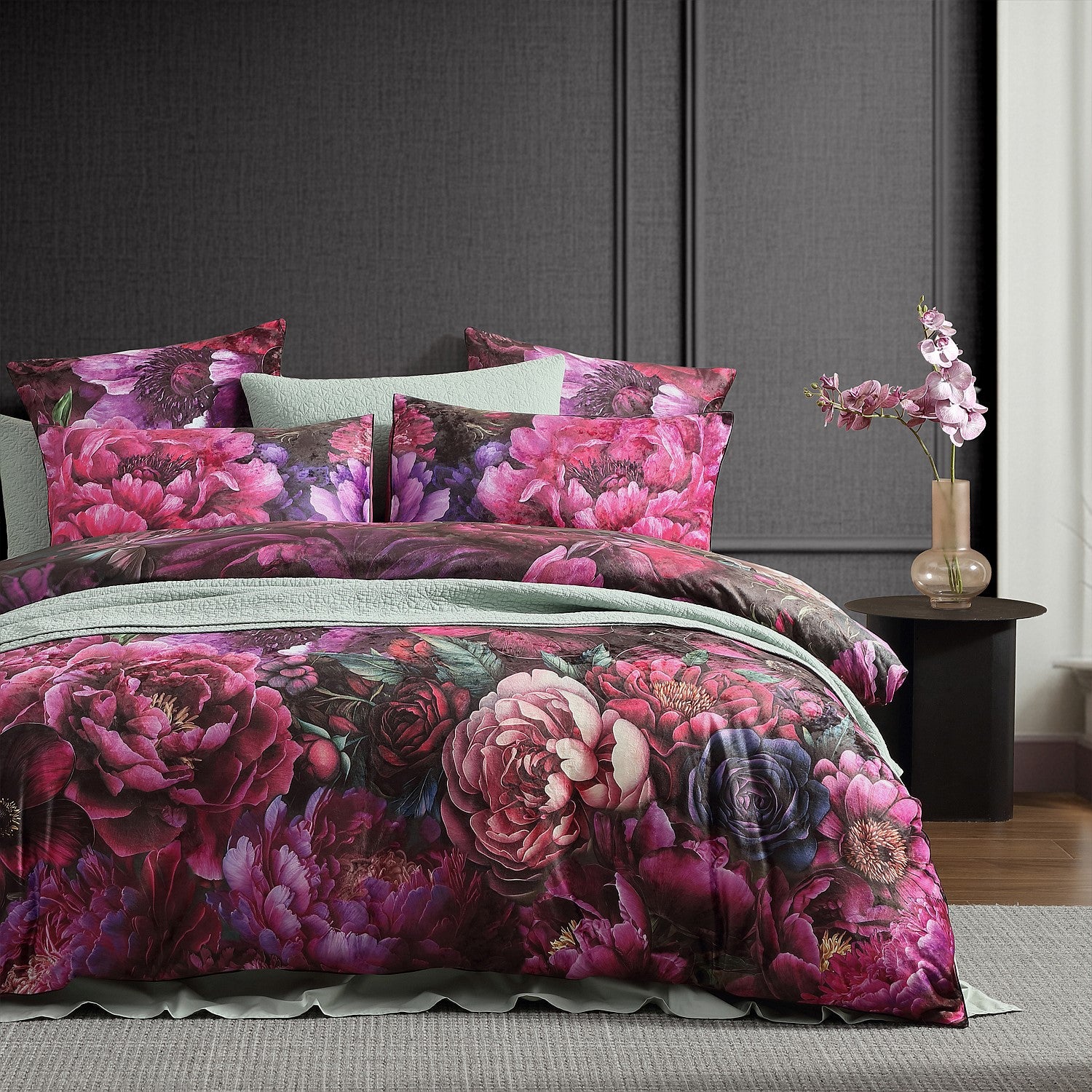 Floral bedding set on a bed with a dark gray wall and side table in the background.