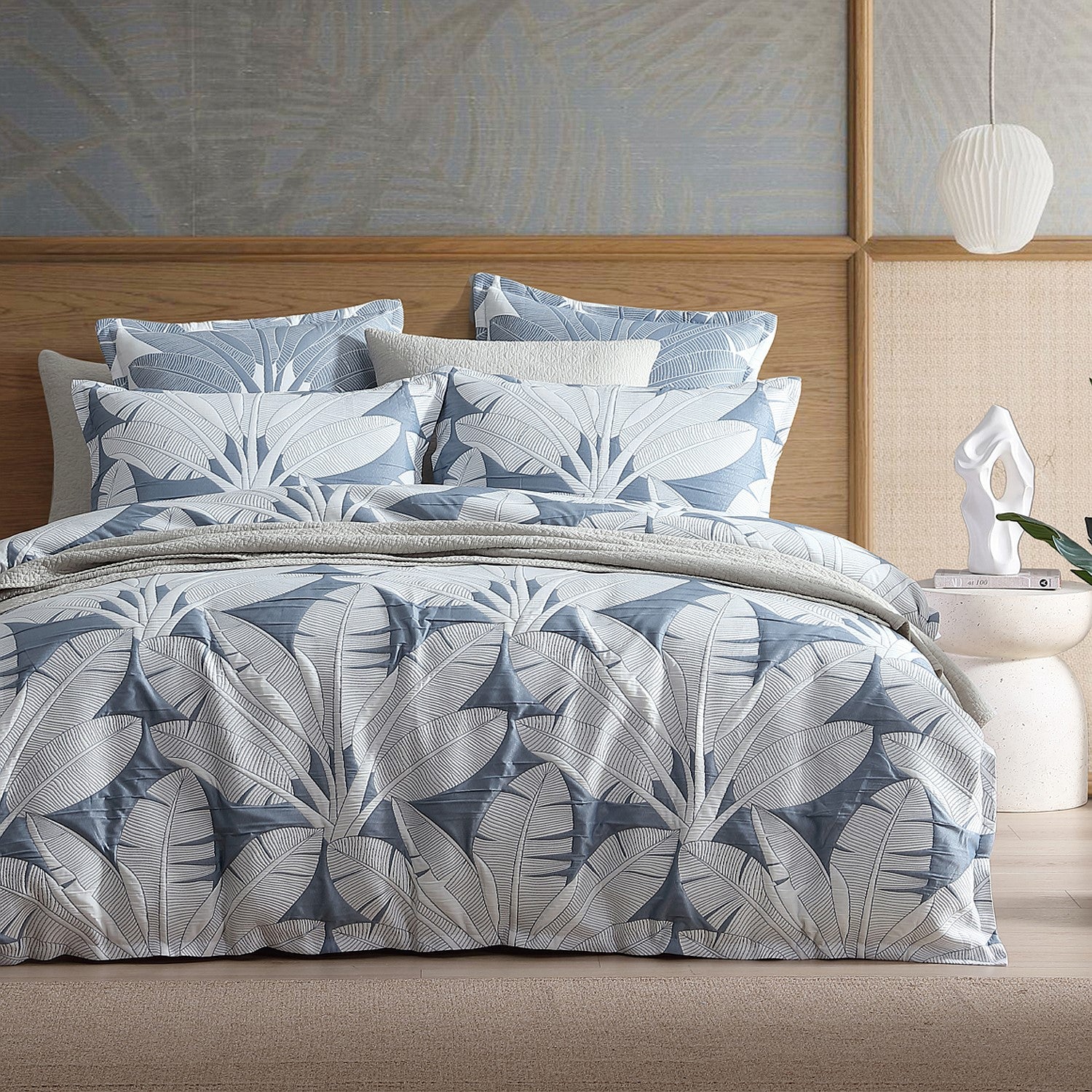 Bed with blue and gray leaf-patterned bedding in a bedroom setting.