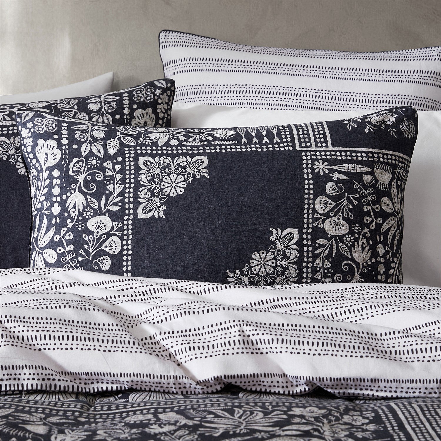 Decorative pillows with black and white patterns on a bed with matching bedding.