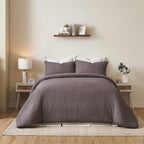 Brown textured duvet cover set on a bed in a bedroom with a shelf and lamp.