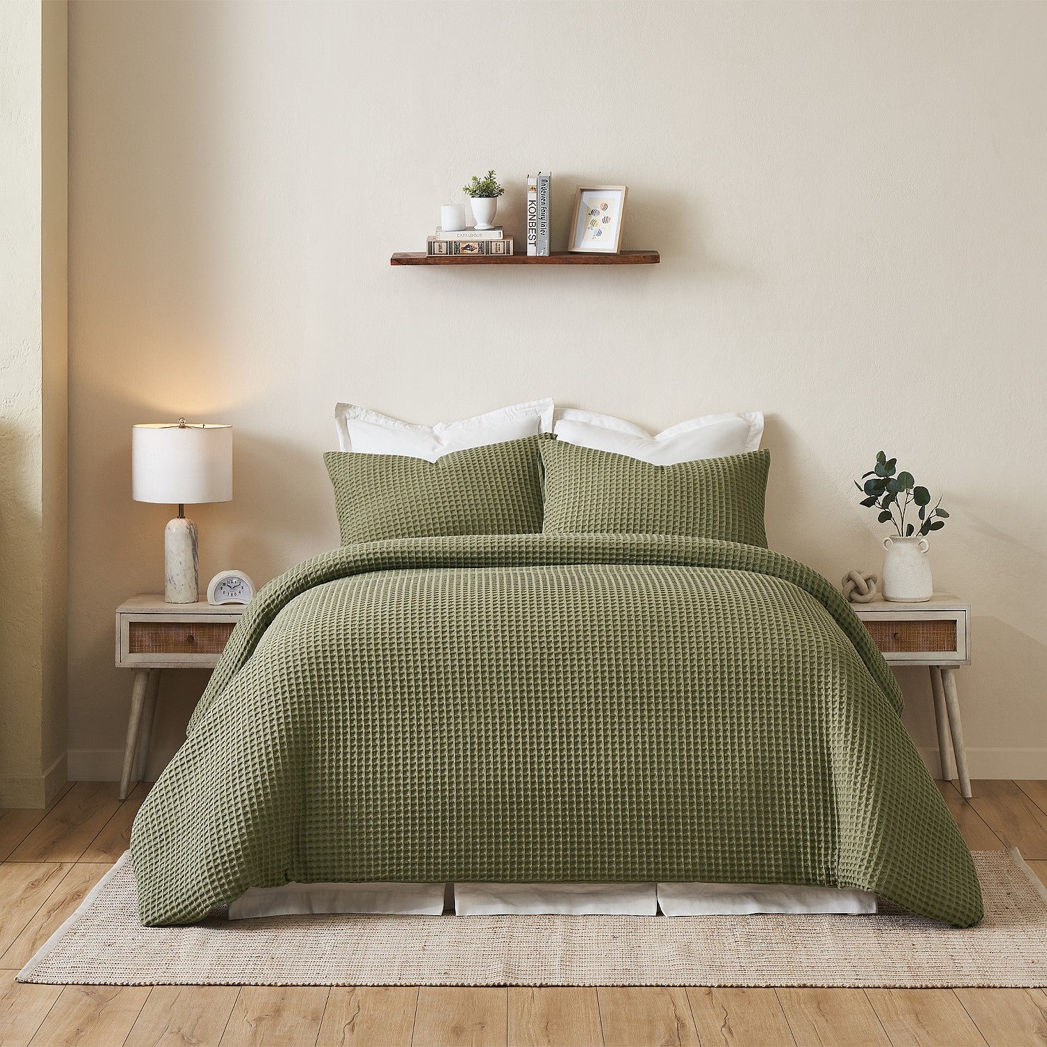 Green textured bedspread on a bed in a bedroom with a shelf and lamp in the background.