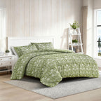 Green patterned comforter set on a bed in a bright bedroom with wooden floor and white walls.