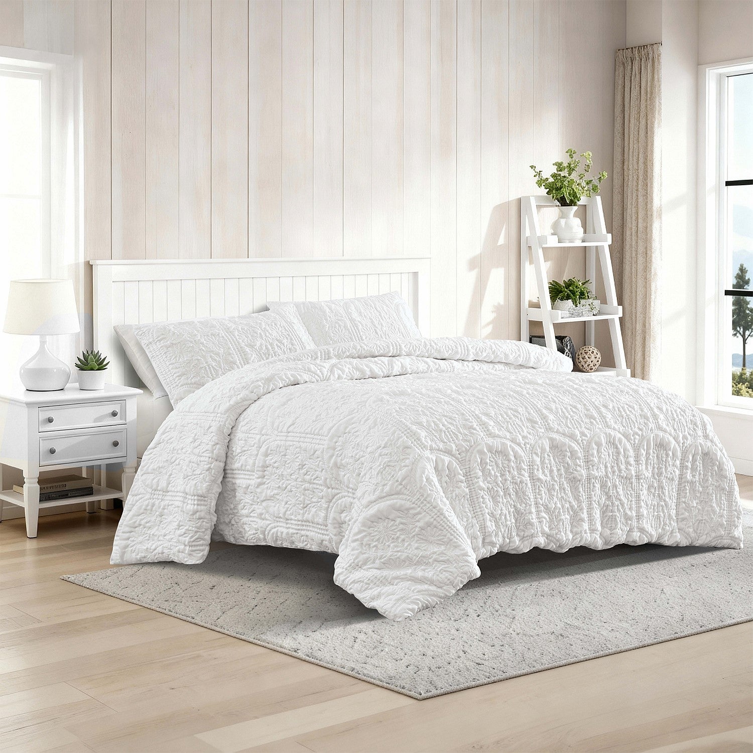 White quilted comforter set on a bed in a bright bedroom with wooden flooring and white walls.