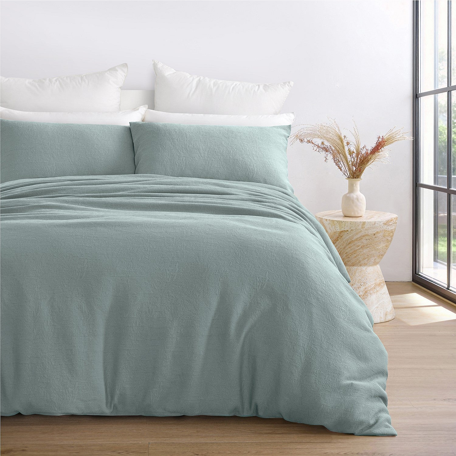 Teal bedding set on a bed with a side table and window in the background