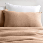 Beige textured comforter and pillows on a bed with a neutral background