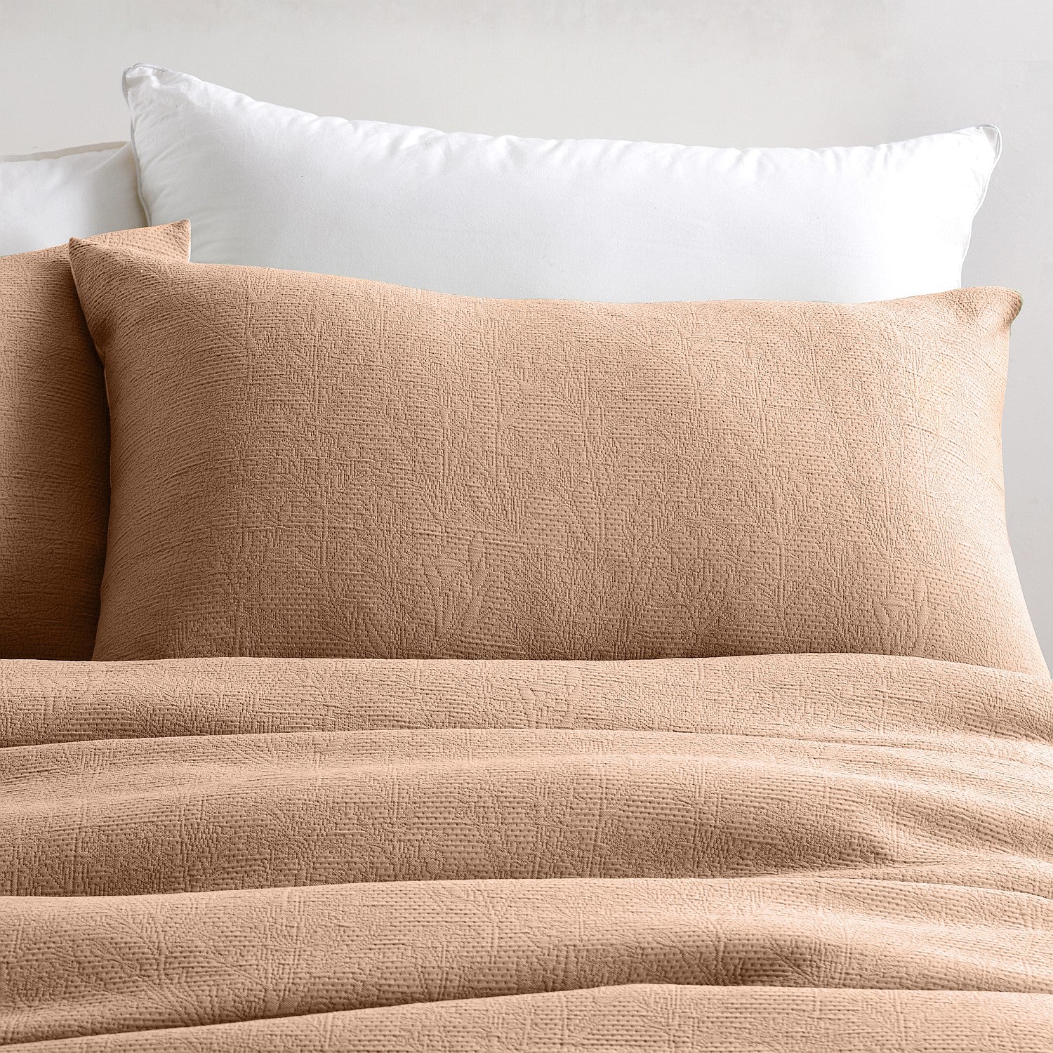 Beige textured comforter and pillows on a bed with a neutral background