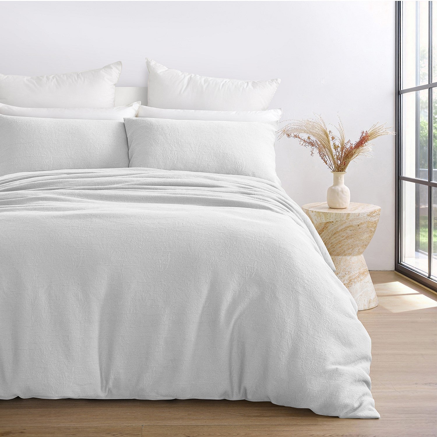 White bedding set on a bed with a side table and window in the background