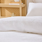 White textured duvet cover on a bed with a wooden headboard and decorative items.