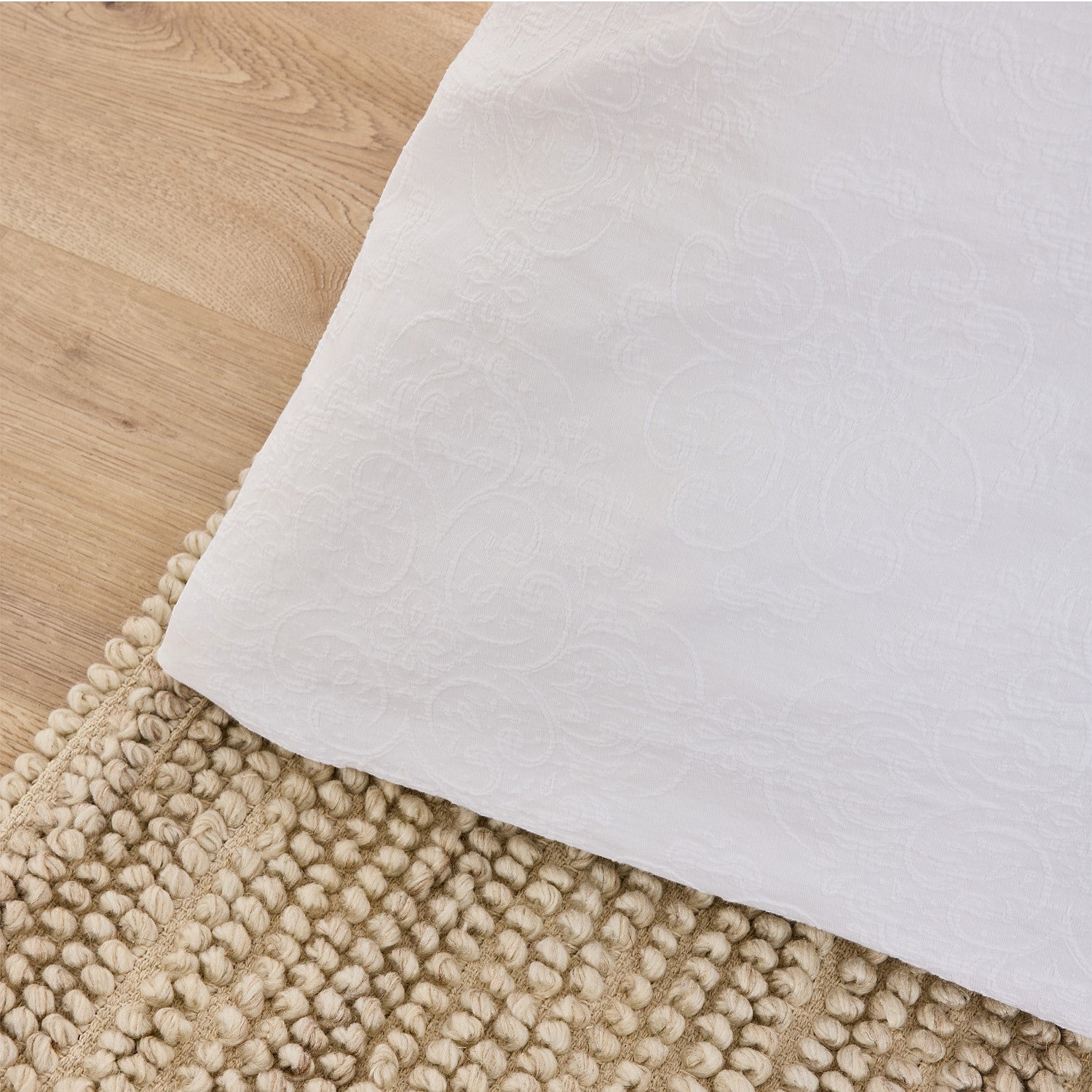 Close-up of a textured beige rug with a white border on a wooden floor.