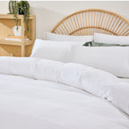 White bedding set on a bed with a wooden headboard and shelf in the background.