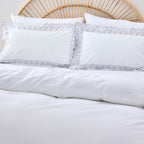 White bedding set with lace trim on a bed with a wicker headboard.