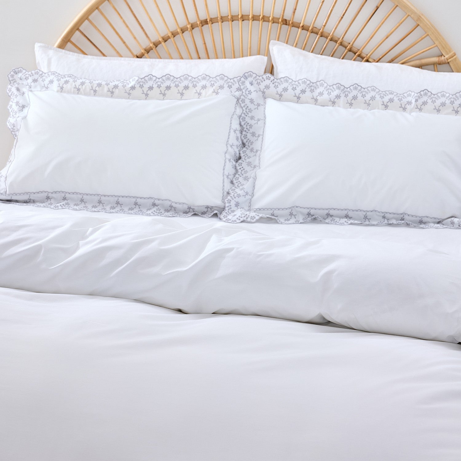 White bedding set with lace trim on a bed with a wicker headboard.
