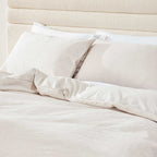 Neatly made bed with white bedding and pillows against a beige headboard.
