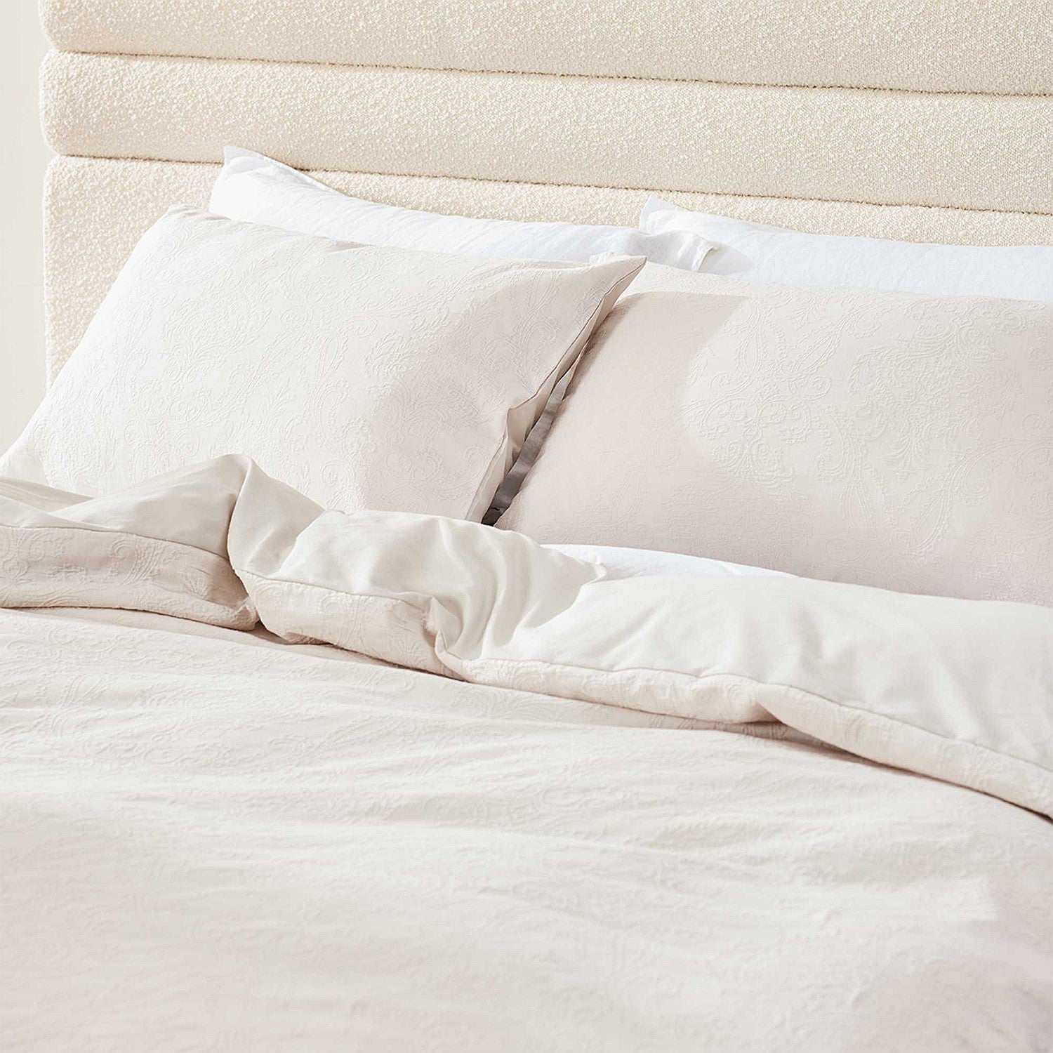 Neatly made bed with white bedding and pillows against a beige headboard.