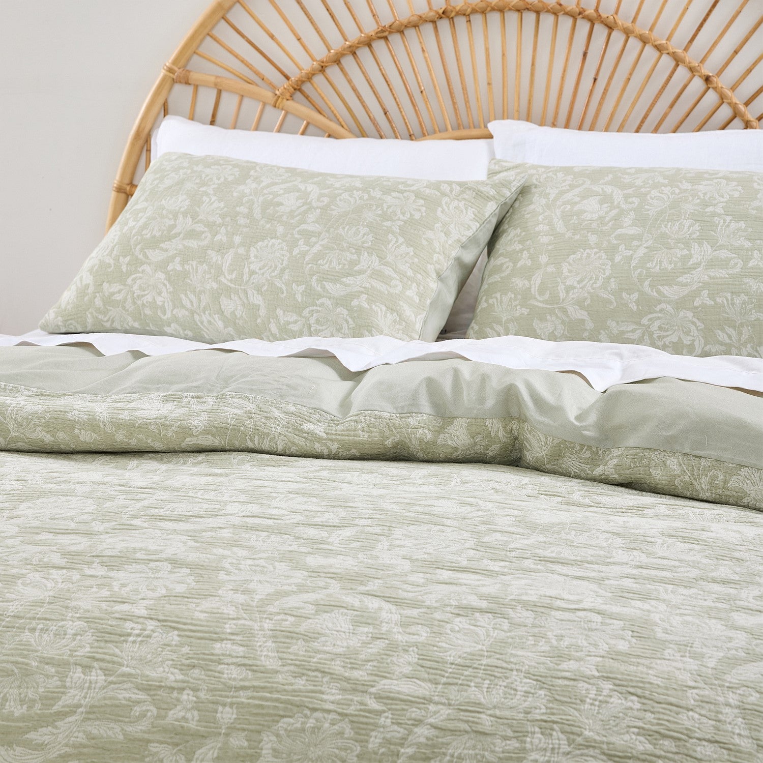 Bed with green floral bedding and a wicker headboard.