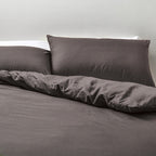 Gray bedding set with pillows on a bed against a neutral background