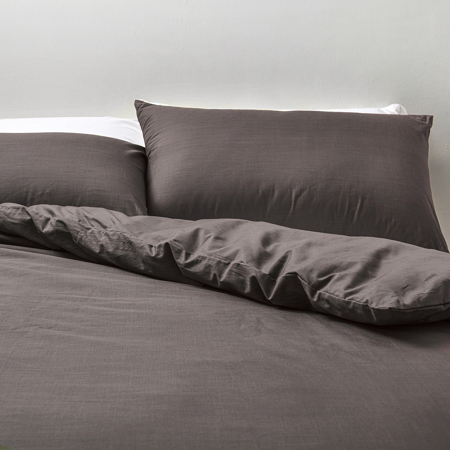 Gray bedding set with pillows on a bed against a neutral background