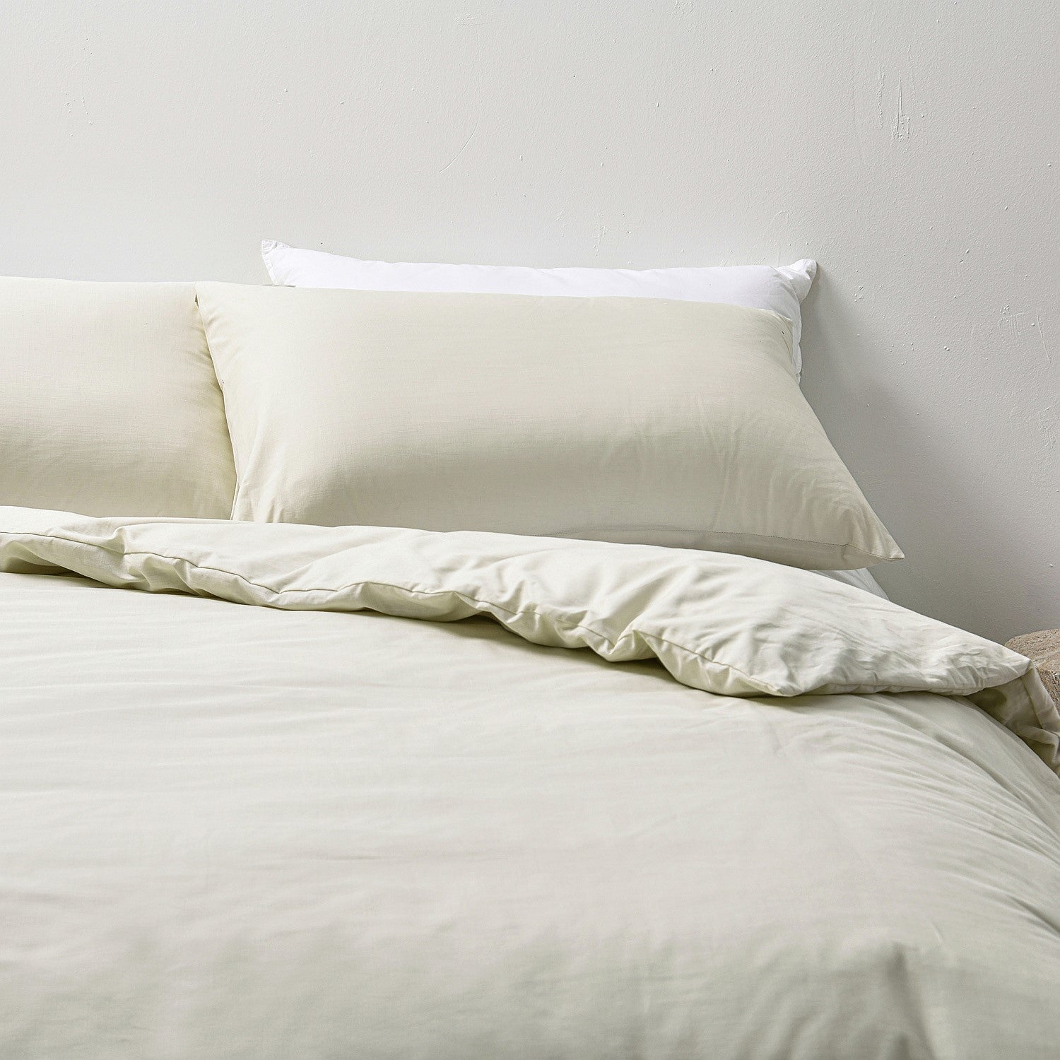 Neatly made bed with white bedding and pillows against a plain wall.
